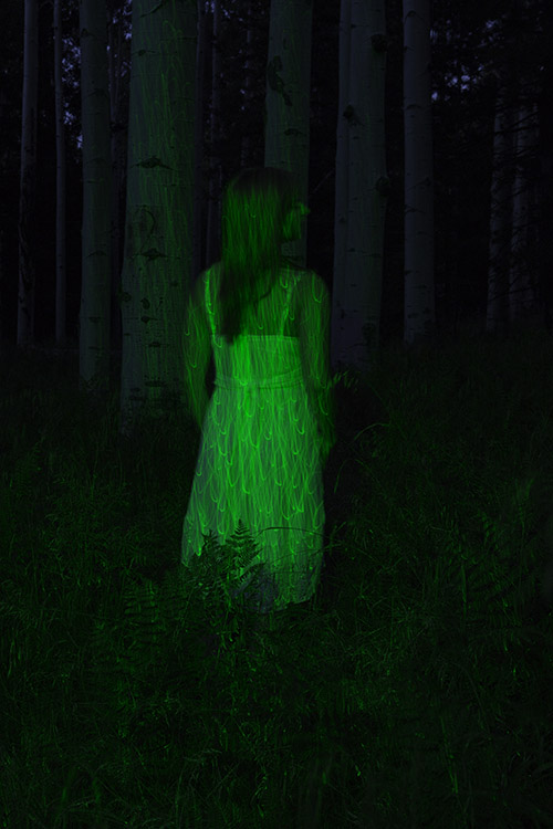 girl lit by green laser in the woods at night